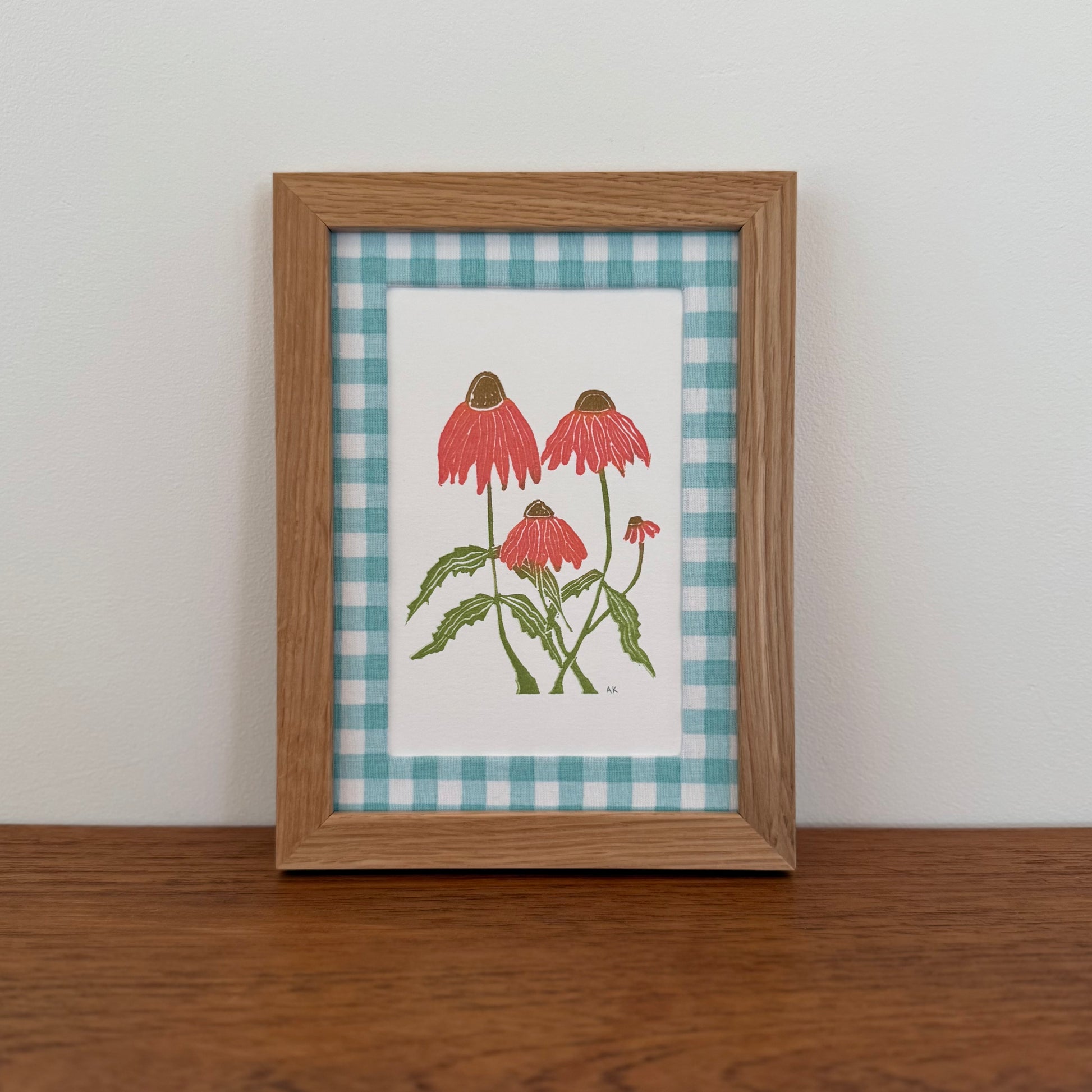 Framed artwork with an echinacea design on a wooden surface and white wall background