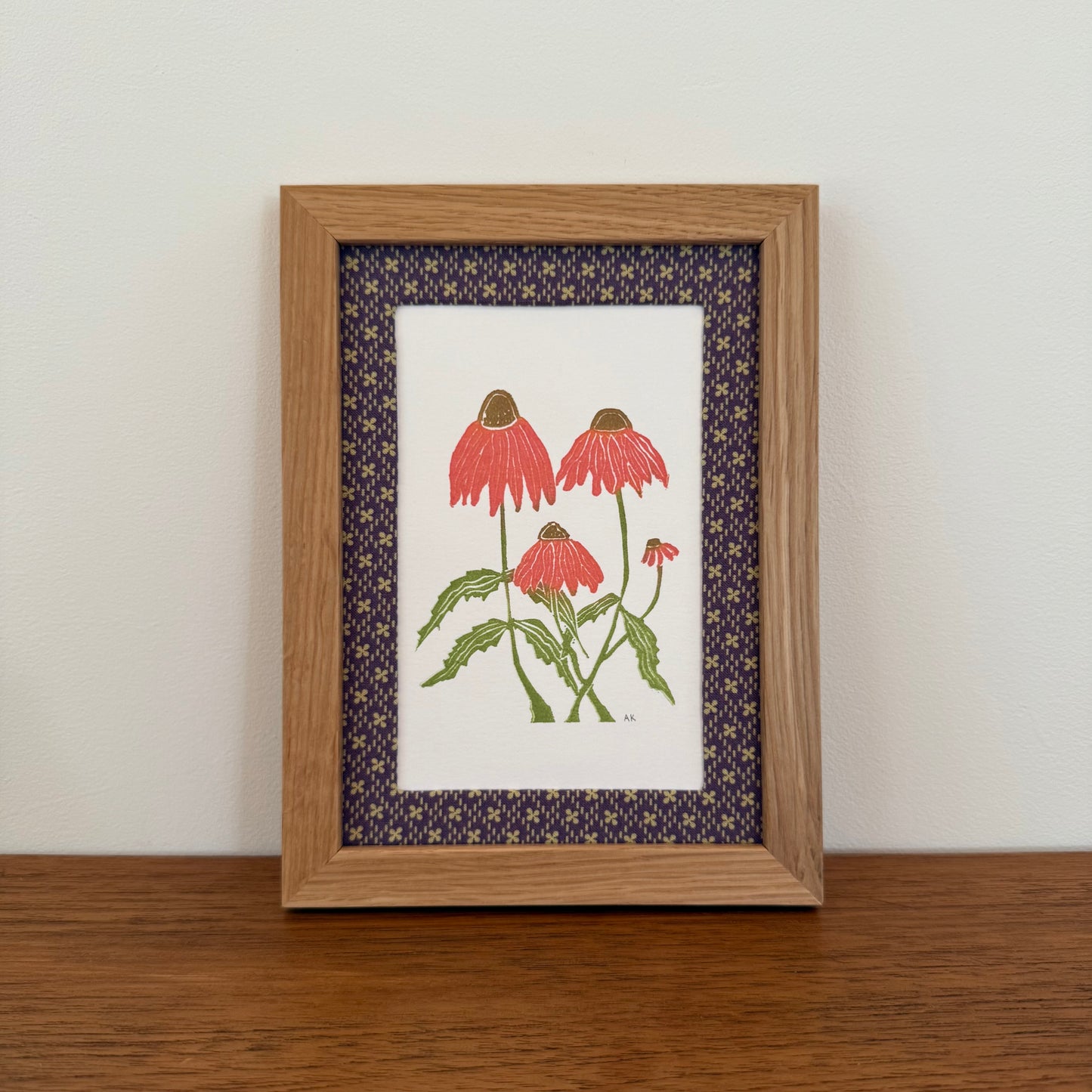 Framed artwork with an echinacea design on a wooden surface and white wall background