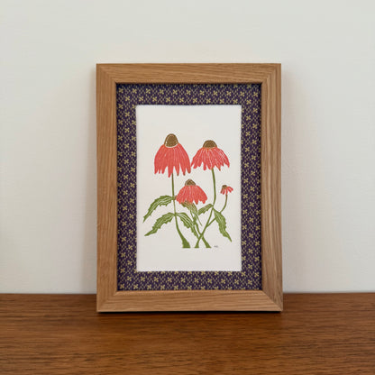 Framed artwork with an echinacea design on a wooden surface and white wall background