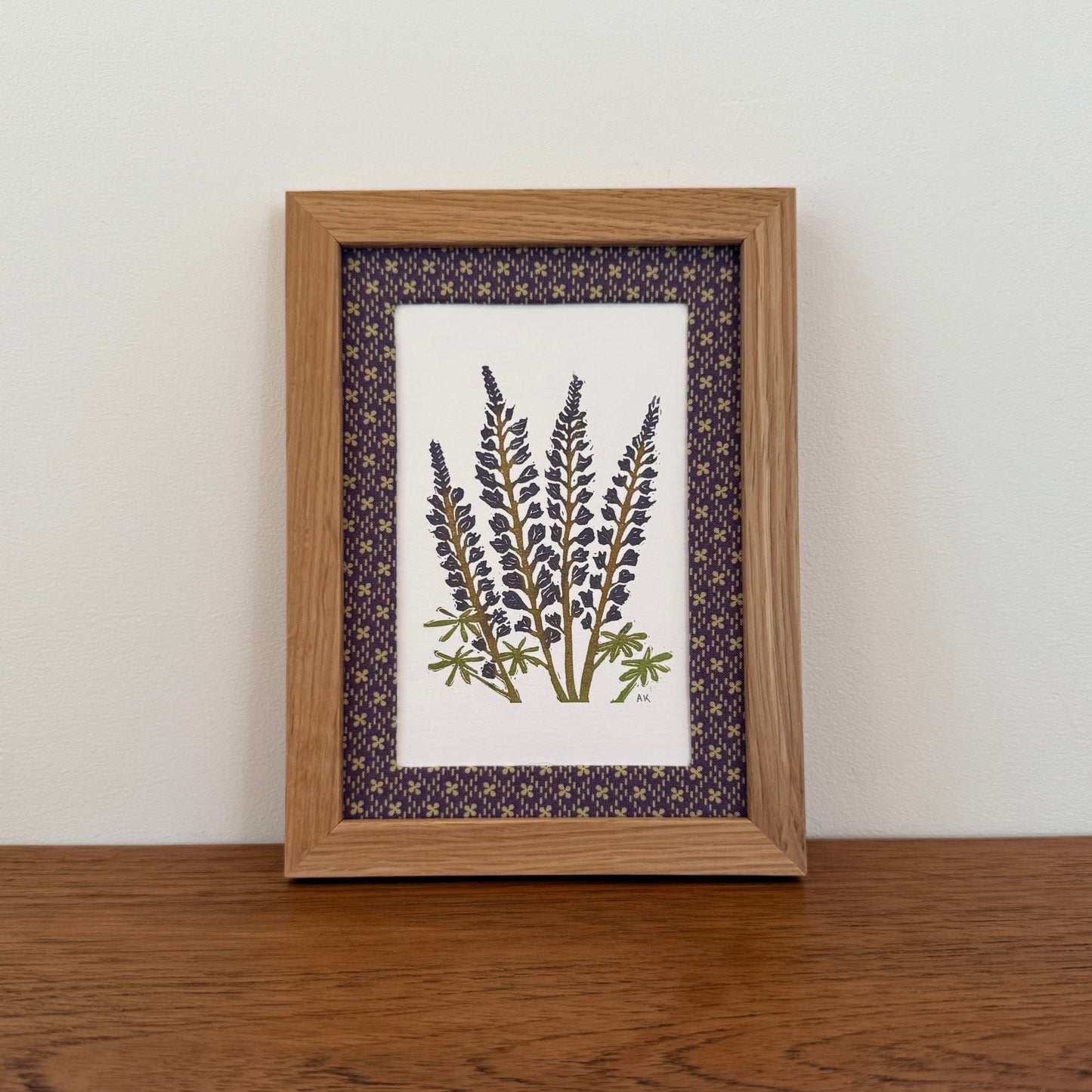 Framed artwork with a lupine design on a wooden surface and white wall background