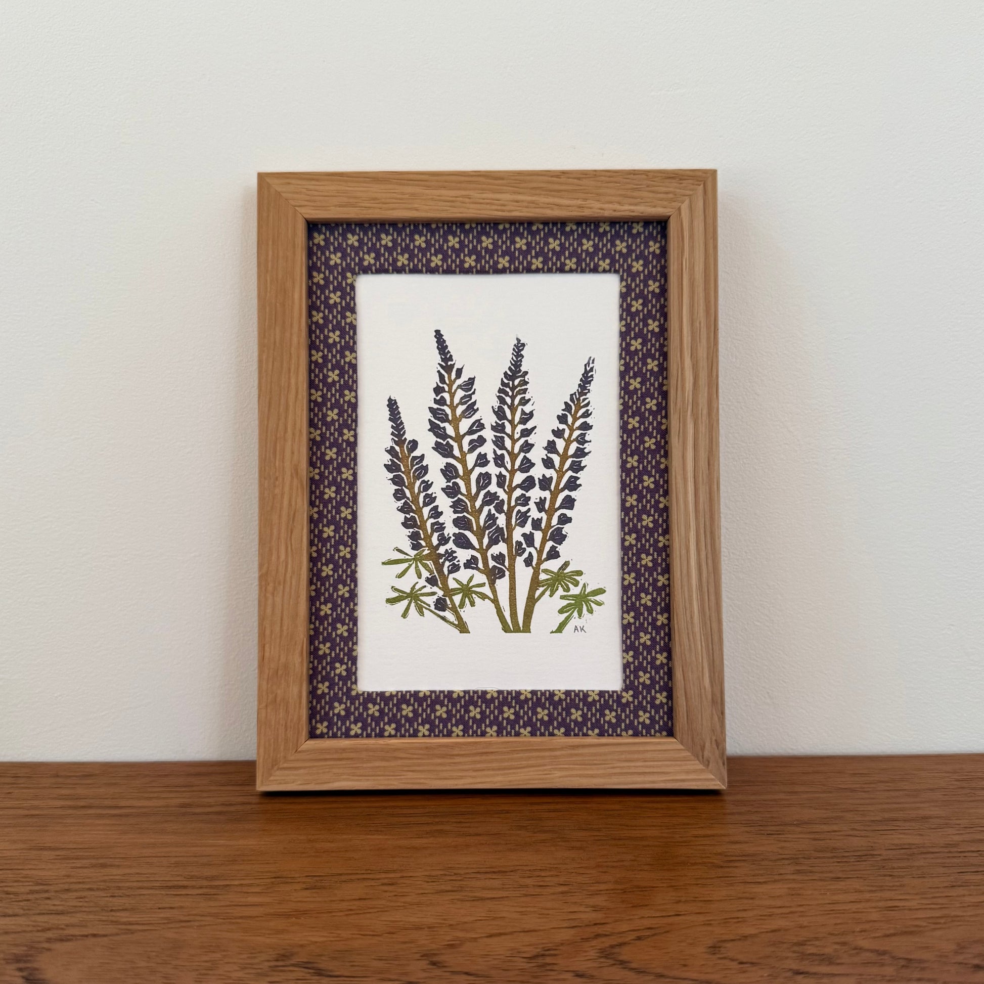 Framed artwork with a lupine design on a wooden surface and white wall background