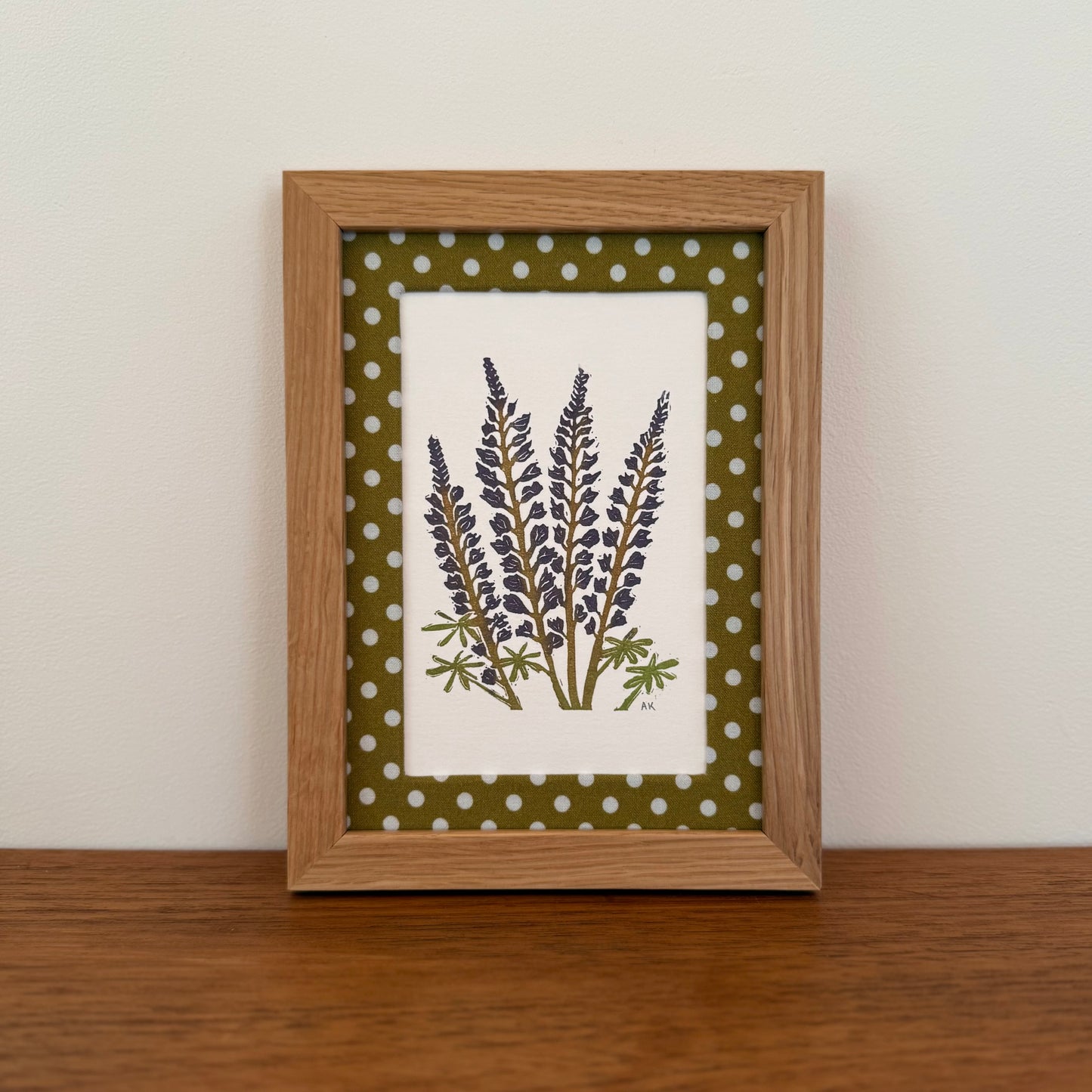 Framed artwork with a lupine design on a wooden surface and white wall background