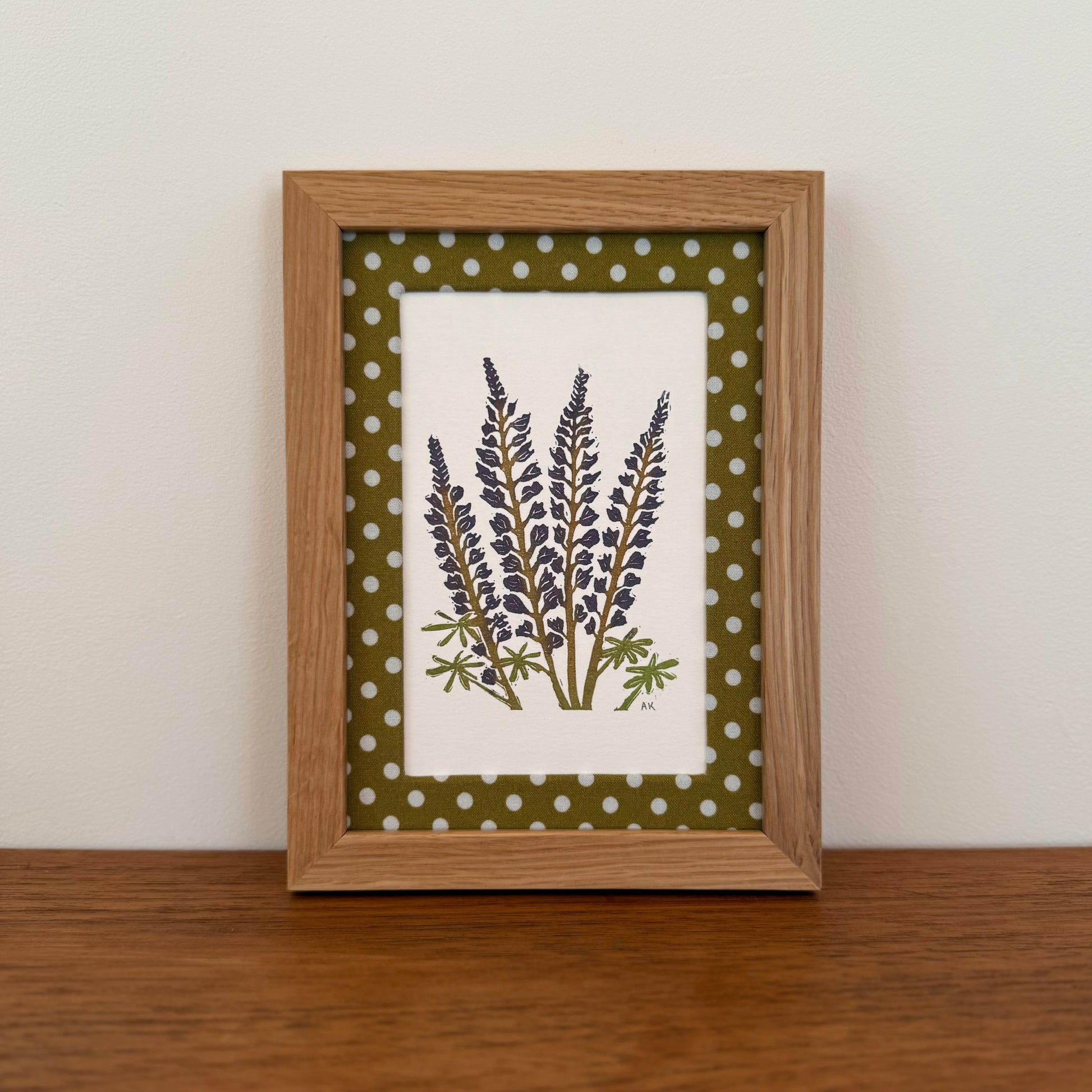 Framed artwork with a lupine design on a wooden surface and white wall background