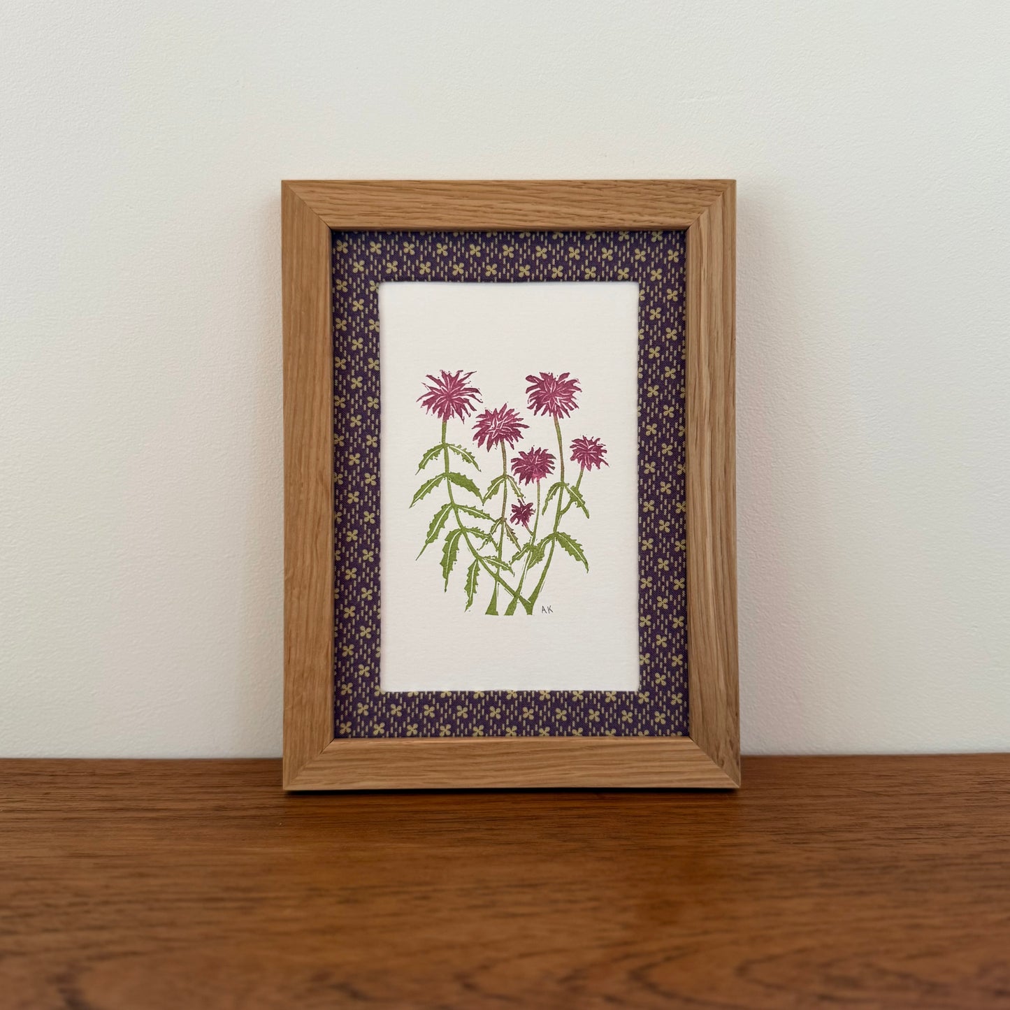 Framed artwork with a bee balm design on a wooden surface and white wall background