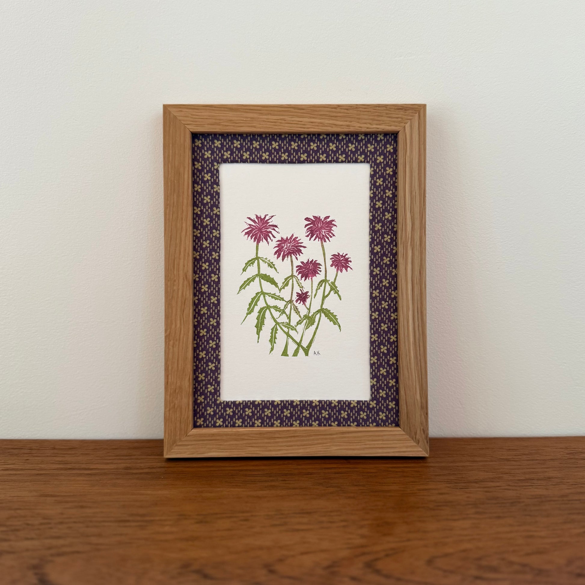 Framed artwork with a bee balm design on a wooden surface and white wall background