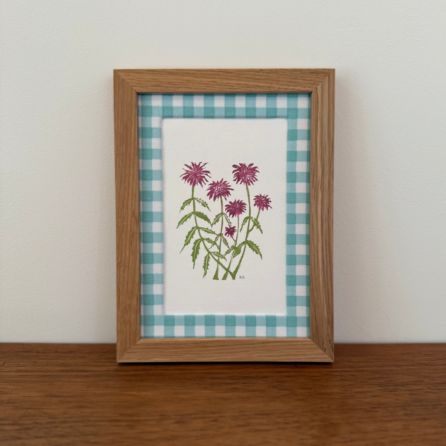 Framed artwork with a bee balm design on a wooden surface and white wall background
