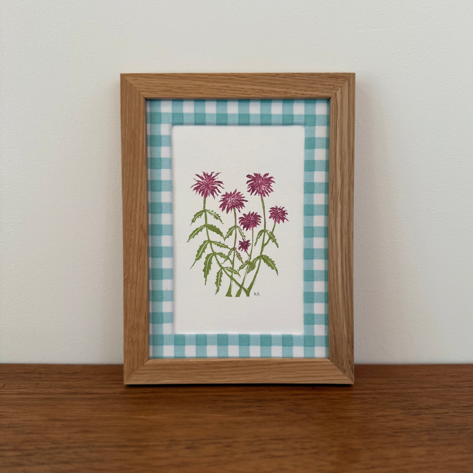 Framed artwork with a bee balm design on a wooden surface and white wall background