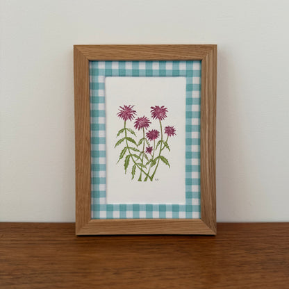 Framed artwork with a bee balm design on a wooden surface and white wall background