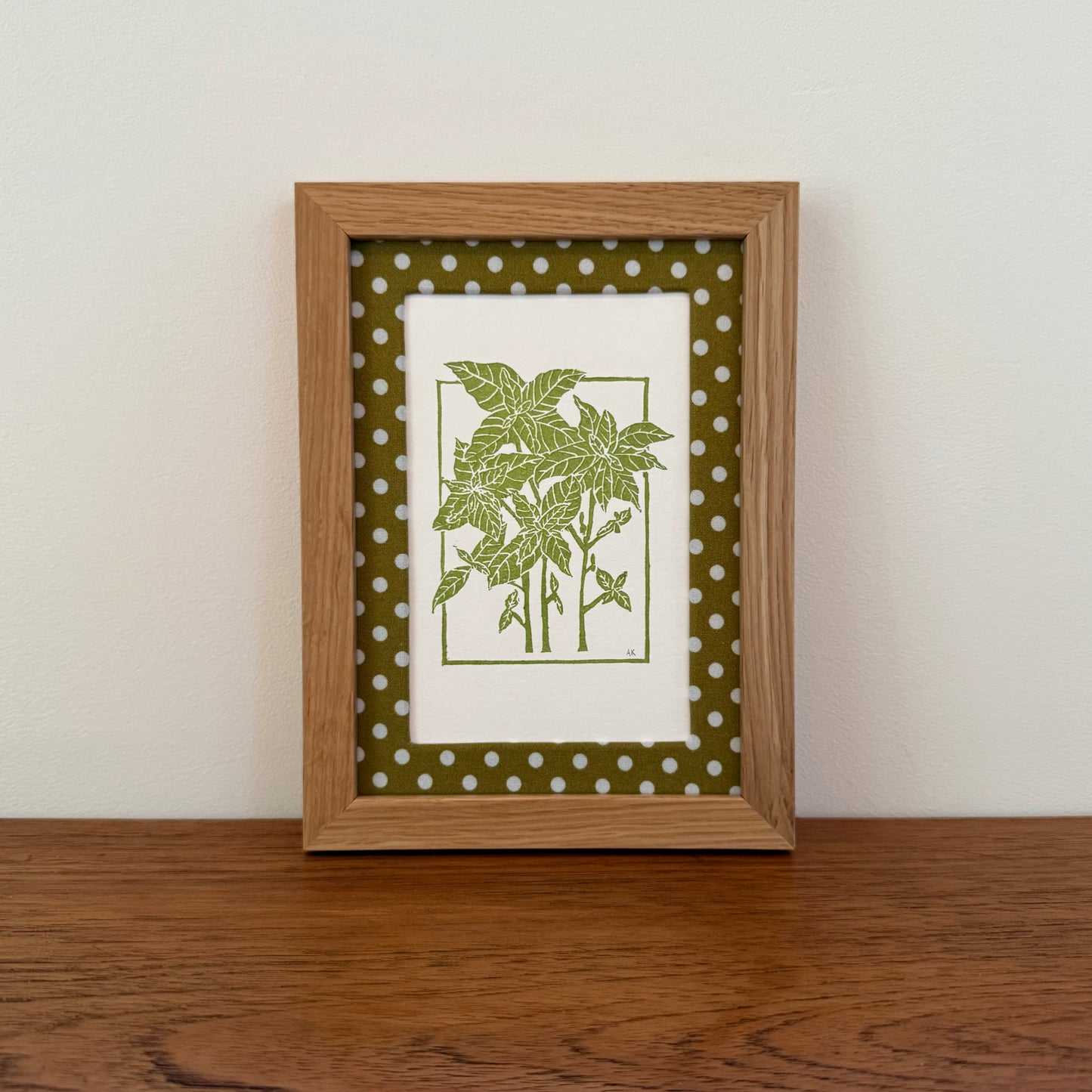 Framed artwork with a basil design on a wooden surface and white wall background