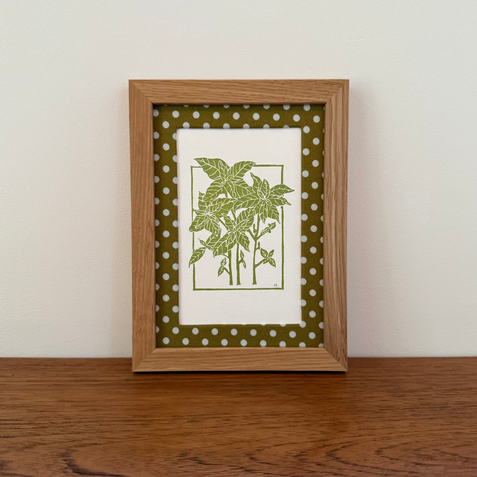 Framed artwork with a basil design on a wooden surface and white wall background