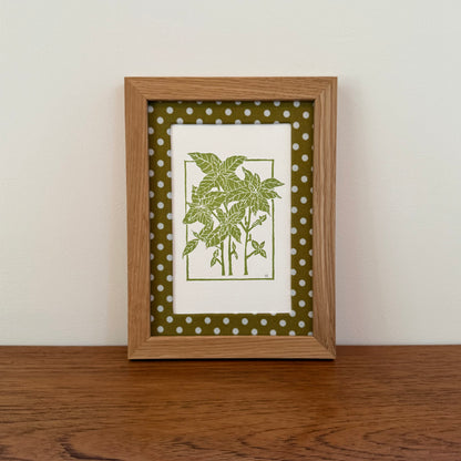 Framed artwork with a basil design on a wooden surface and white wall background