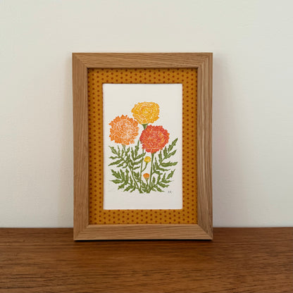 Framed artwork with a marigold design on a wooden surface and white wall background