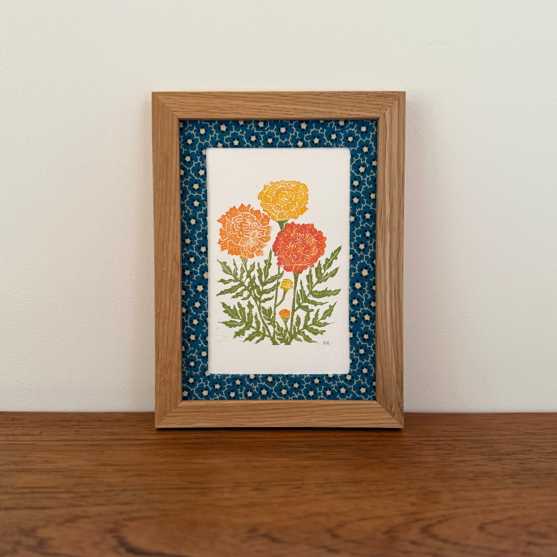 Framed artwork with a marigold design on a wooden surface and white wall background