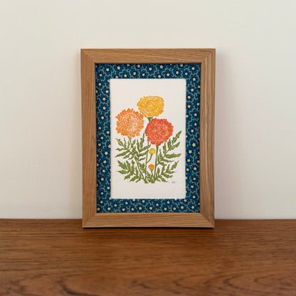 Framed artwork with a marigold design on a wooden surface and white wall background
