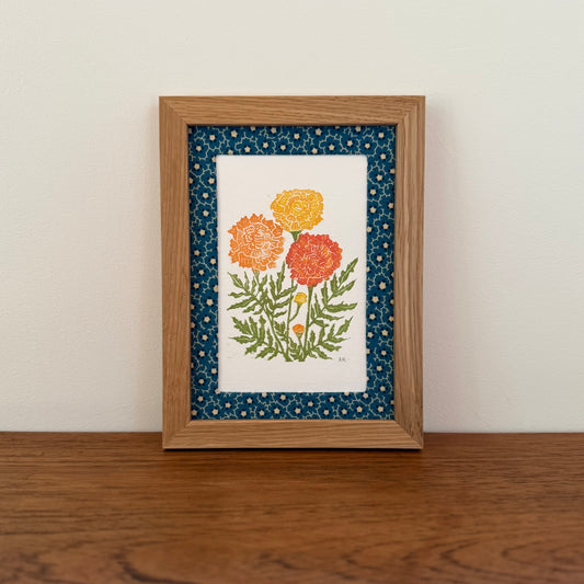 Framed artwork with a marigold design on a wooden surface and white wall background
