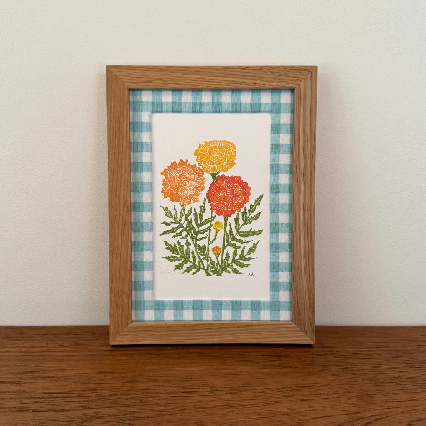 Framed artwork with a marigold design on a wooden surface and white wall background