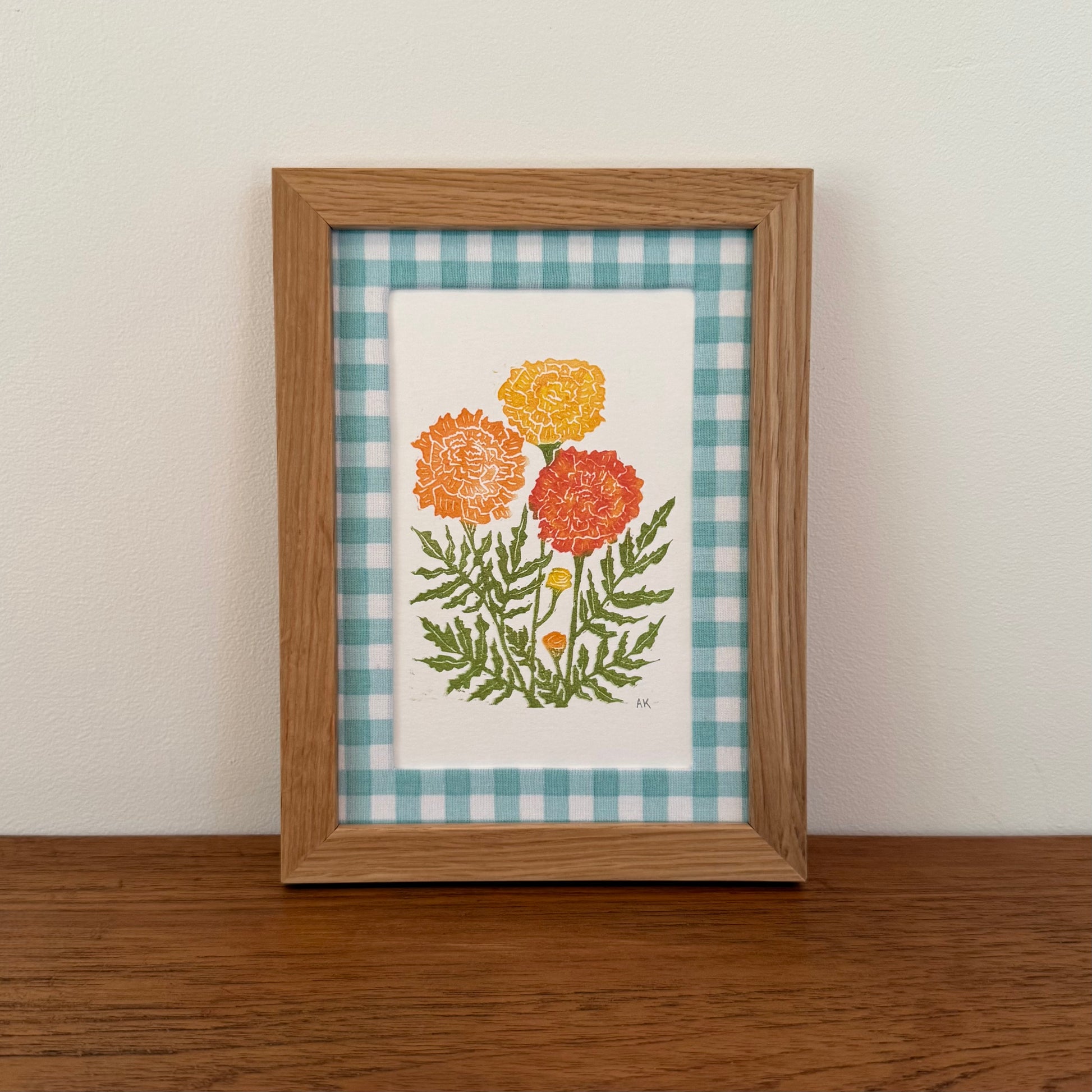 Framed artwork with a marigold design on a wooden surface and white wall background