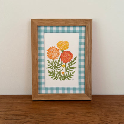 Framed artwork with a marigold design on a wooden surface and white wall background