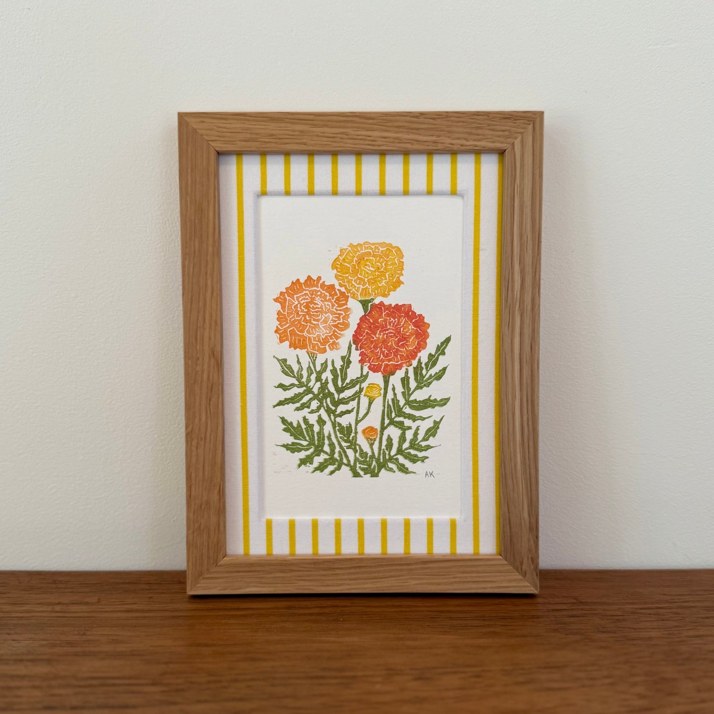 Framed artwork with a marigold design on a wooden surface and white wall background
