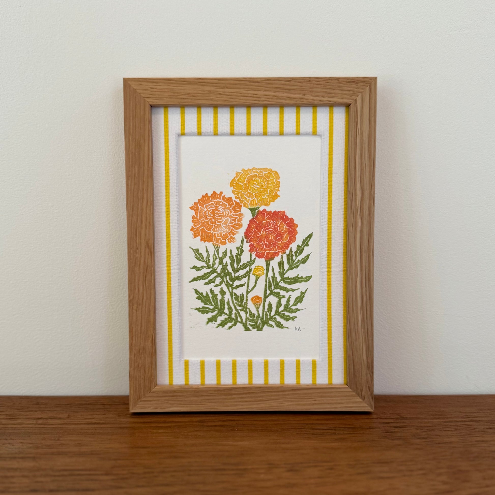 Framed artwork with a marigold design on a wooden surface and white wall background