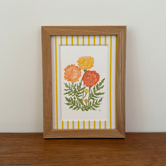 Framed artwork with a marigold design on a wooden surface and white wall background