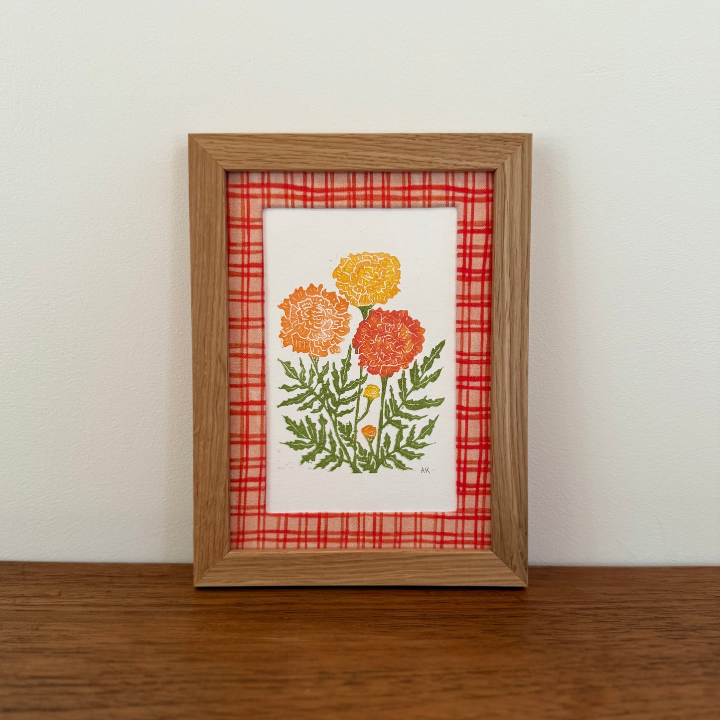 Framed artwork with a marigold design on a wooden surface and white wall background