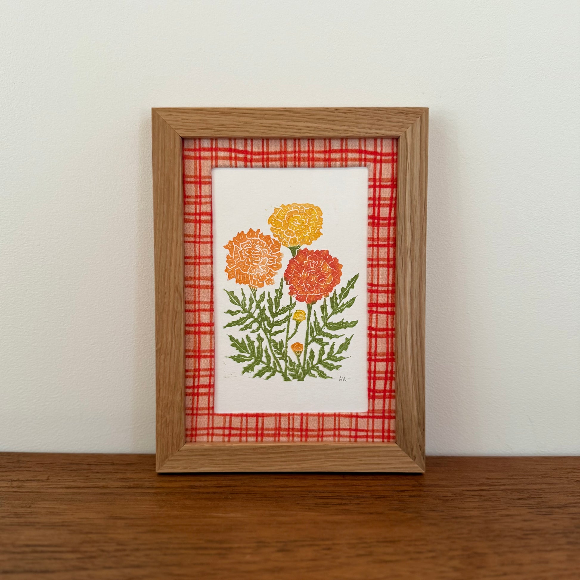 Framed artwork with a marigold design on a wooden surface and white wall background