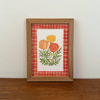 Framed artwork with a marigold design on a wooden surface and white wall background