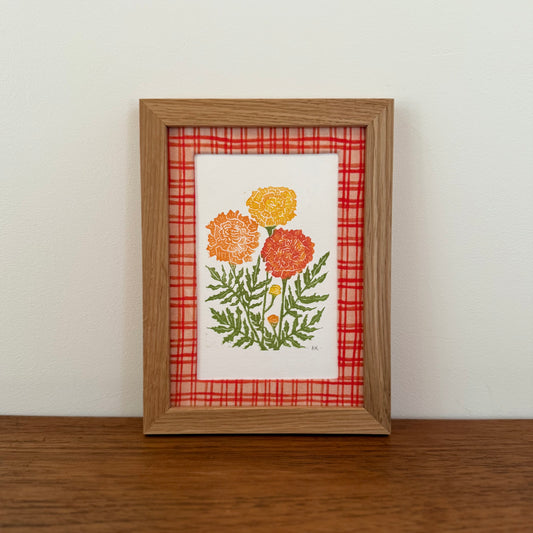Framed artwork with a marigold design on a wooden surface and white wall background