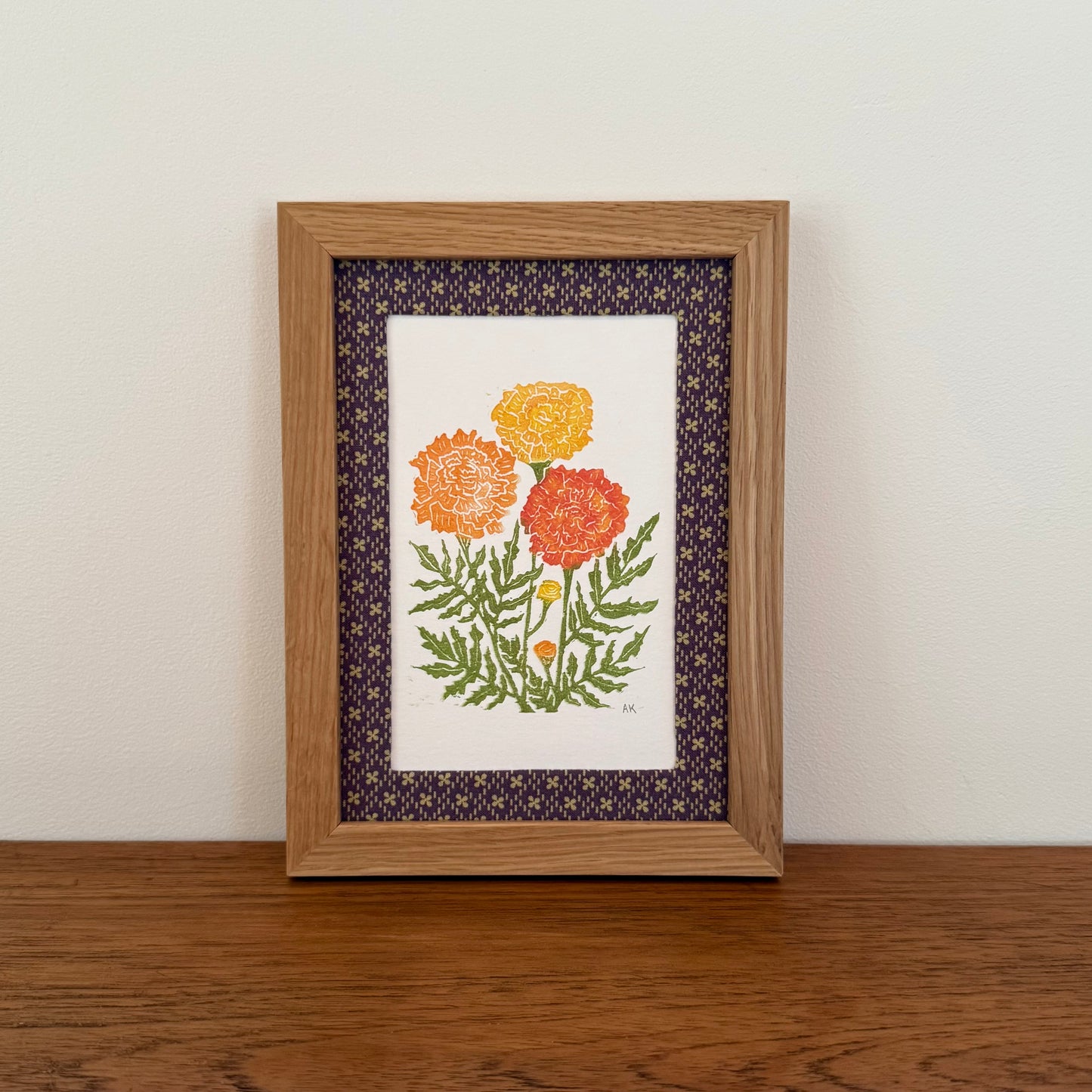 Framed artwork with a marigold design on a wooden surface and white wall background