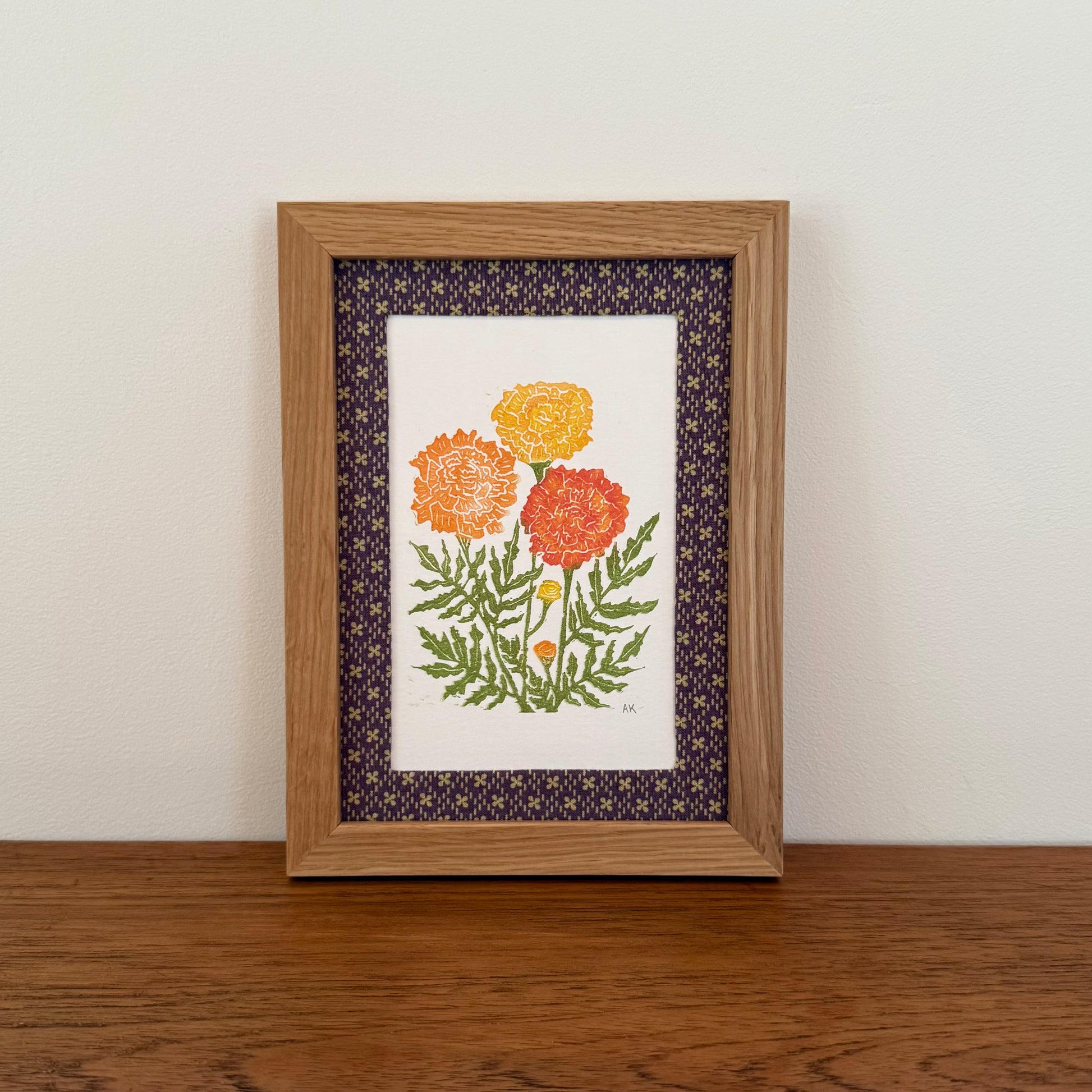 Framed artwork with a marigold design on a wooden surface and white wall background
