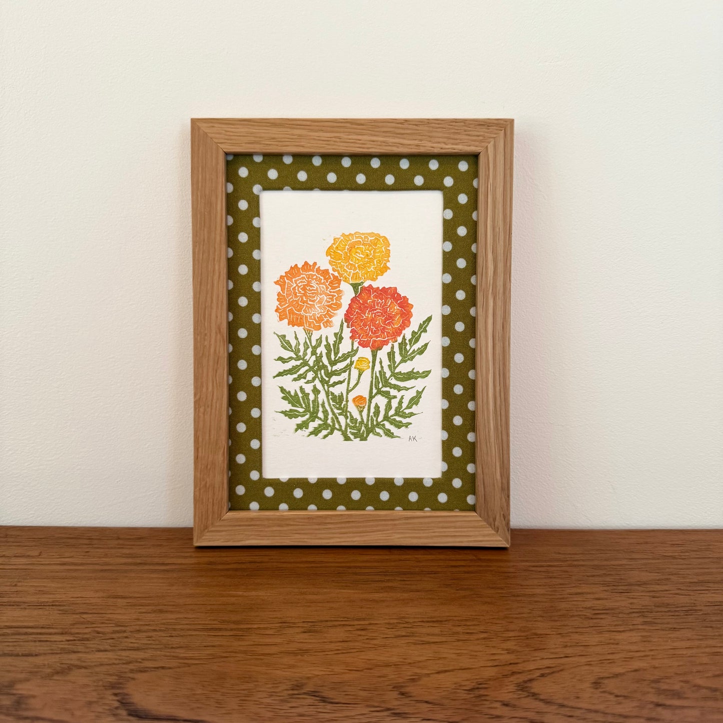 Framed artwork with a marigold design on a wooden surface and white wall background