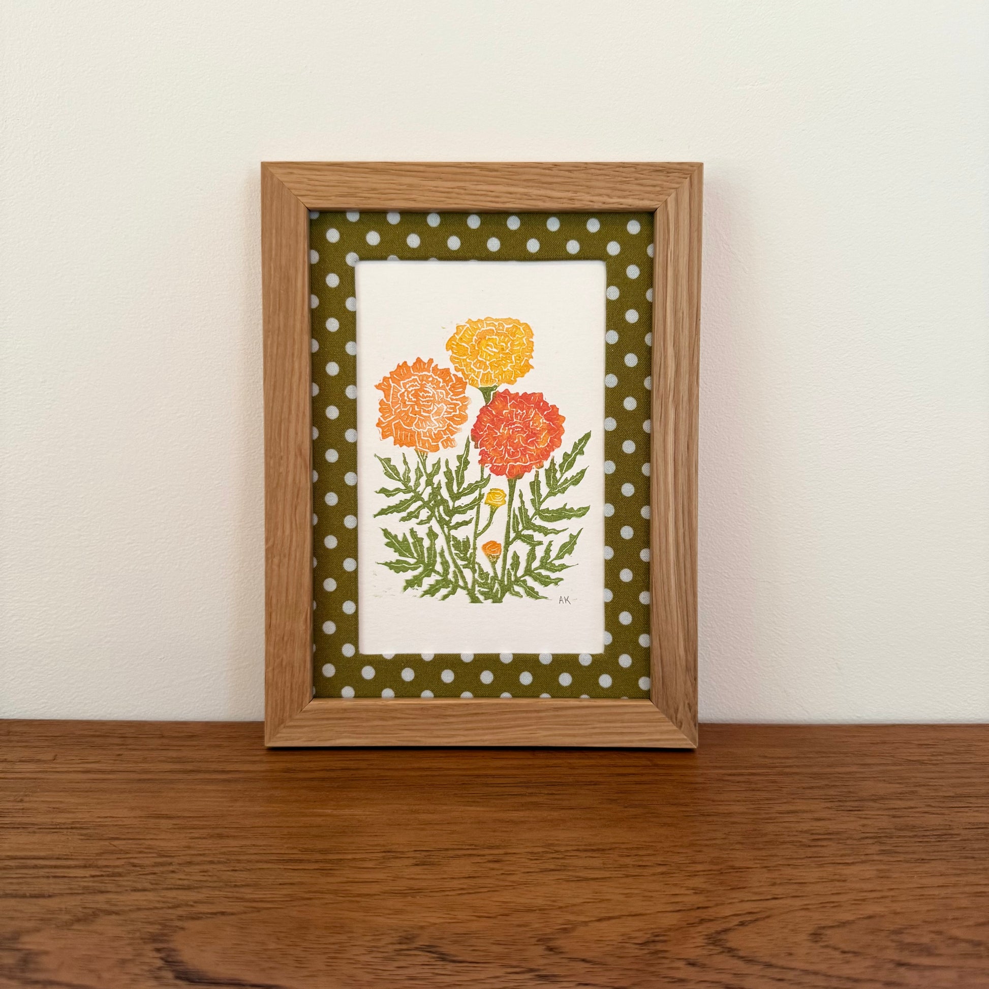 Framed artwork with a marigold design on a wooden surface and white wall background