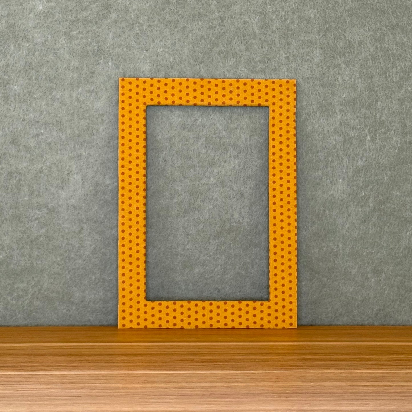 Yellow and rust colored polka dot photo mat sitting on a wooden surface with a gray wall background.