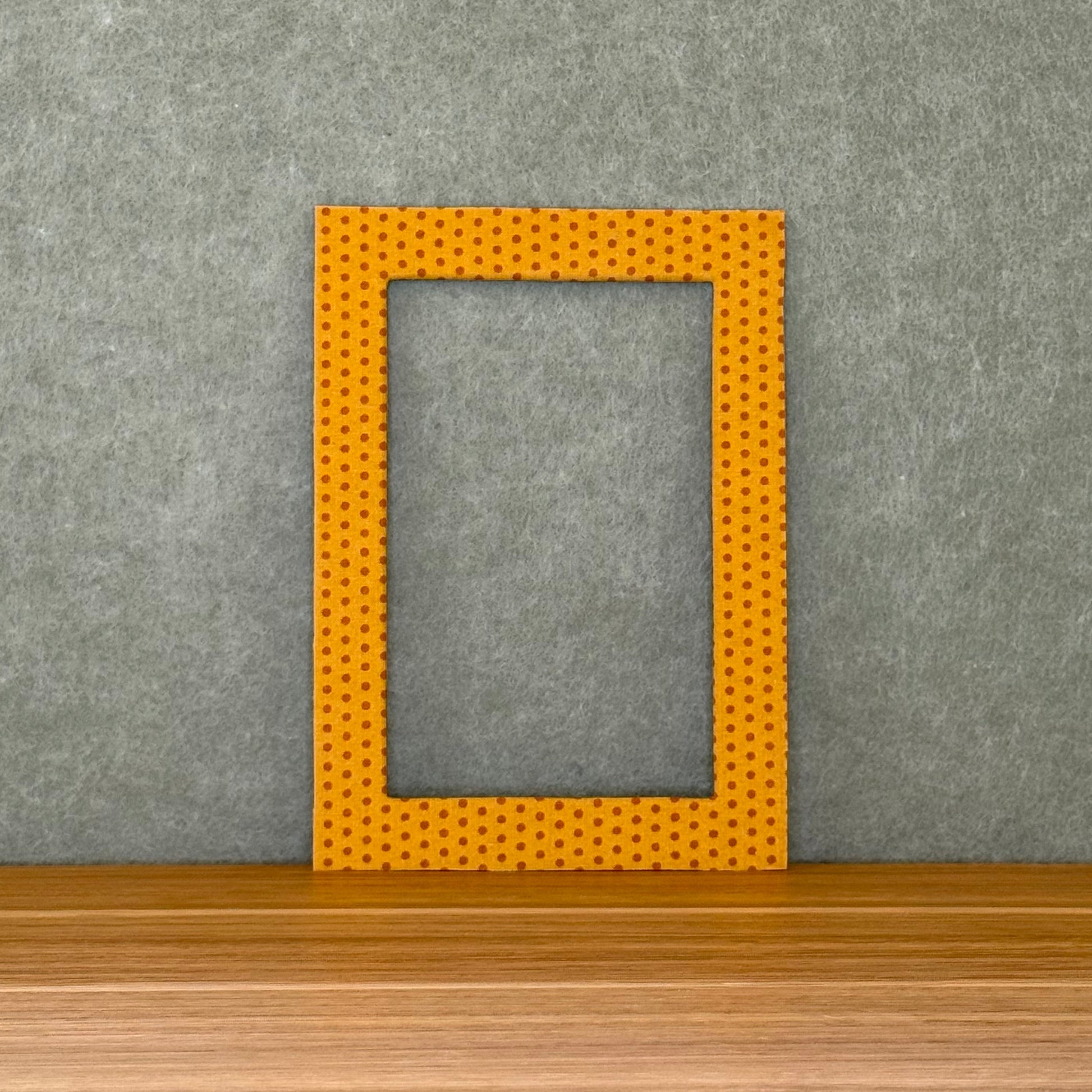 Yellow and rust colored polka dot photo mat sitting on a wooden surface with a gray wall background.