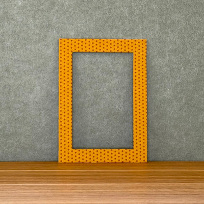 Yellow and rust colored polka dot photo mat sitting on a wooden surface with a gray wall background.