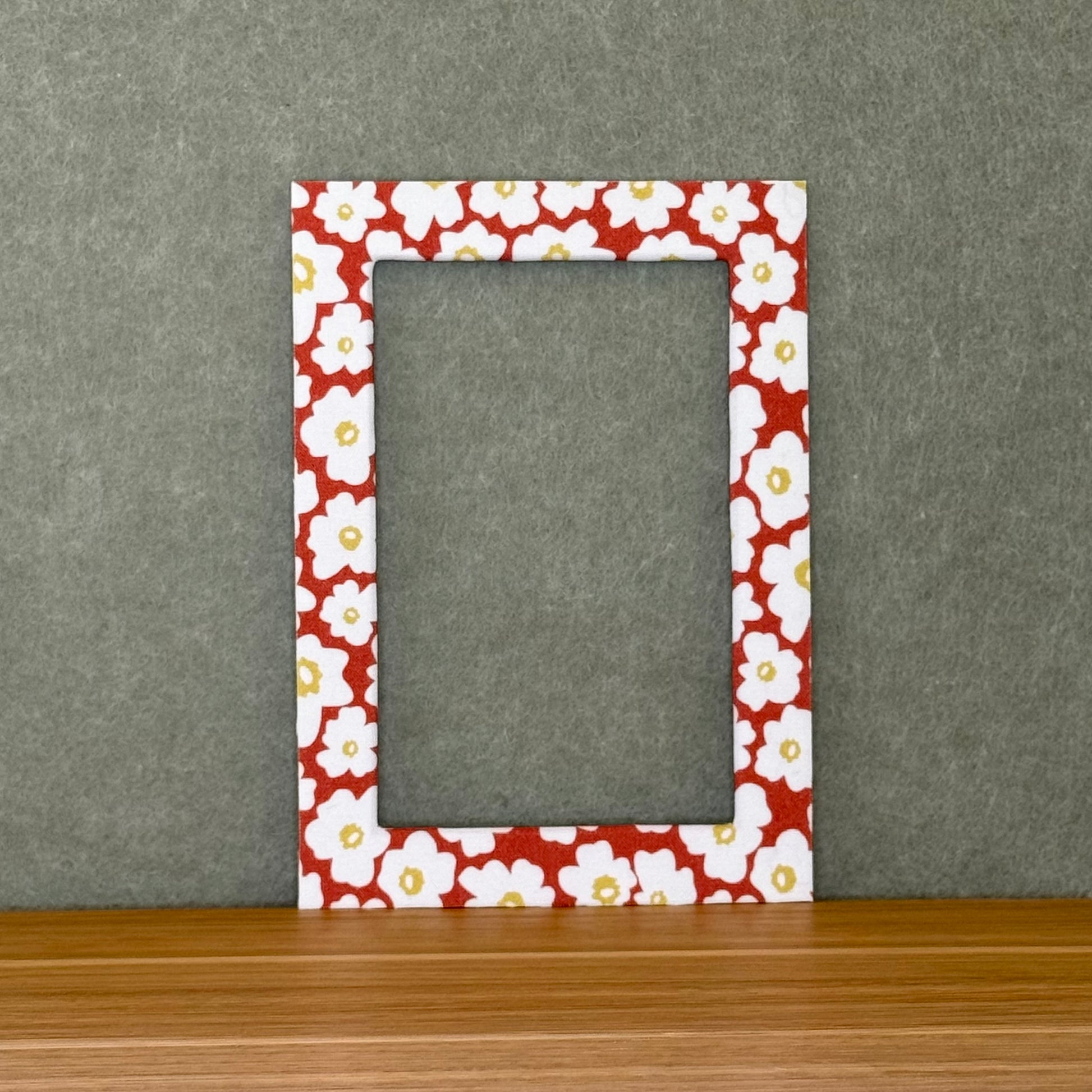 Red, white and yellow floral patterned photo mat on a wooden surface with a gray background