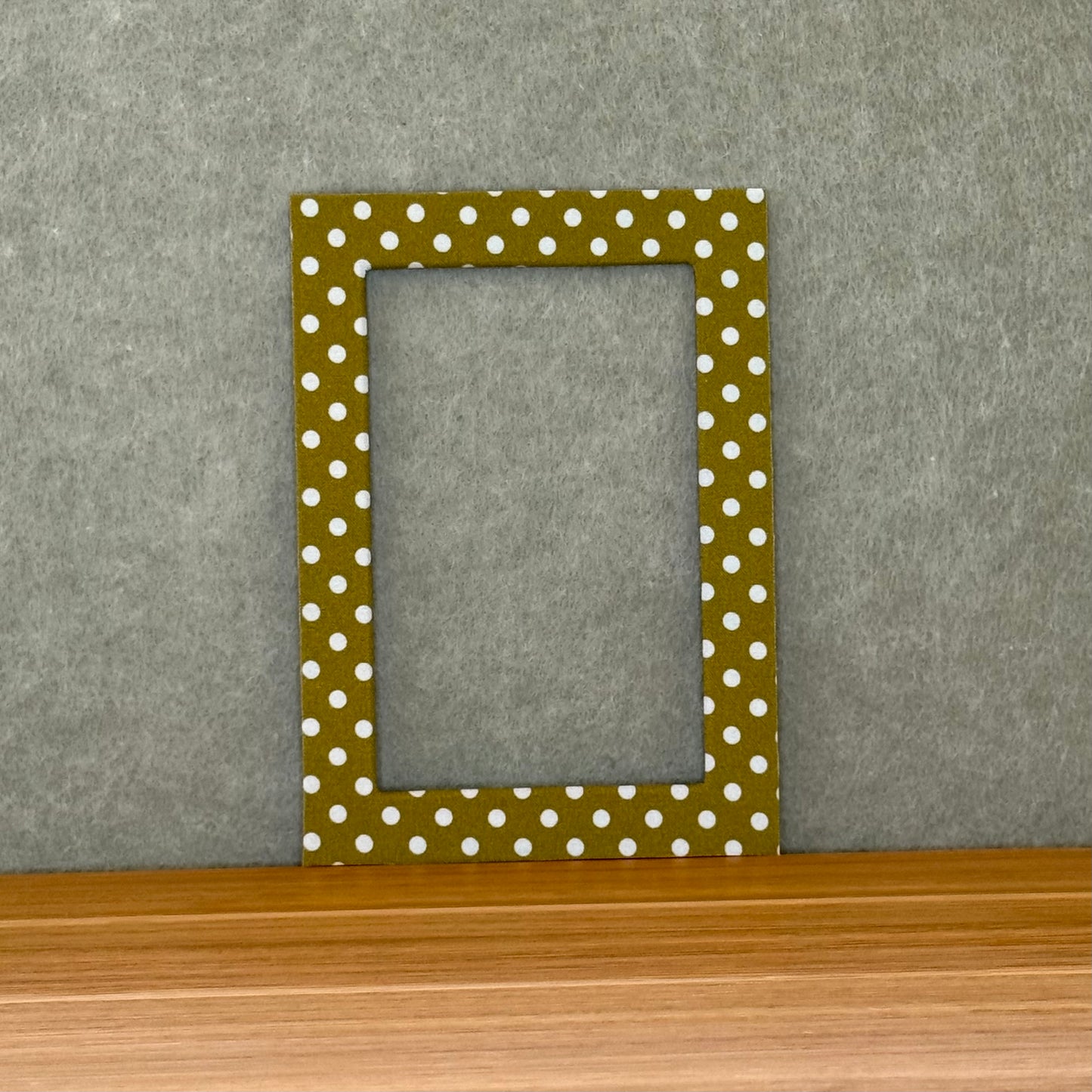 Green photo mat with white polka dots on a wooden surface and gray wall background
