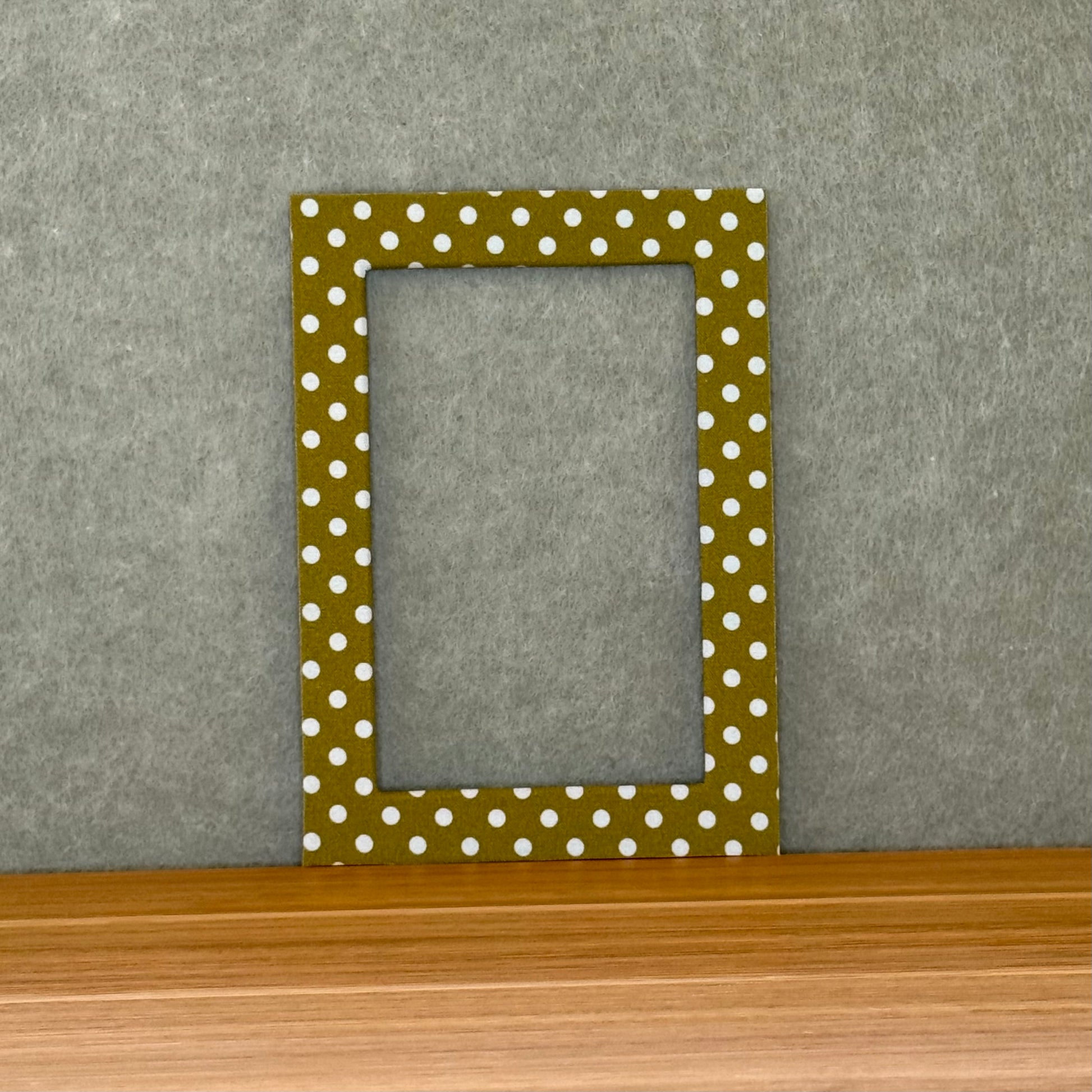 Green photo mat with white polka dots on a wooden surface and gray wall background