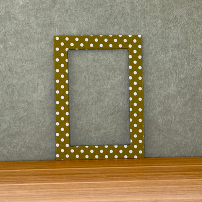 Green photo mat with white polka dots on a wooden surface and gray wall background