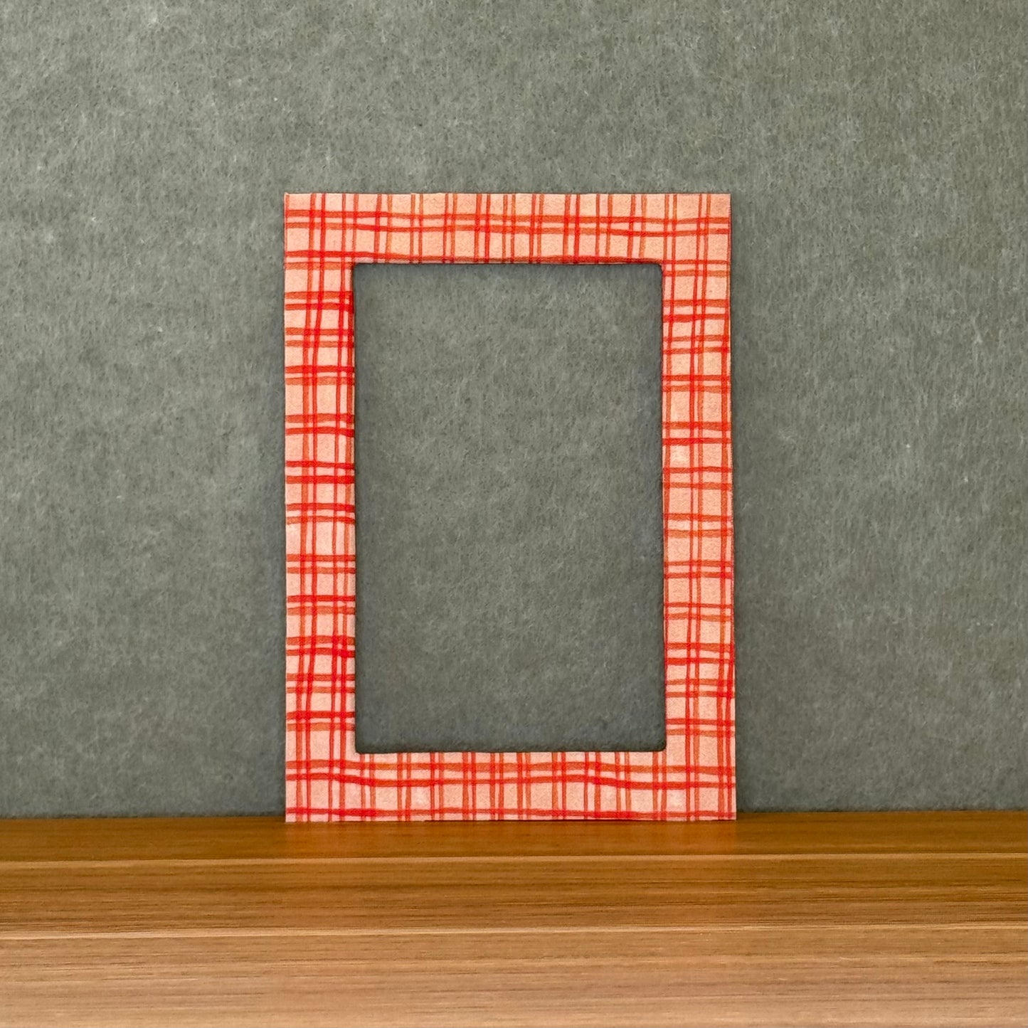 Red plaid photo mat on a wooden surface with a gray wall background. 