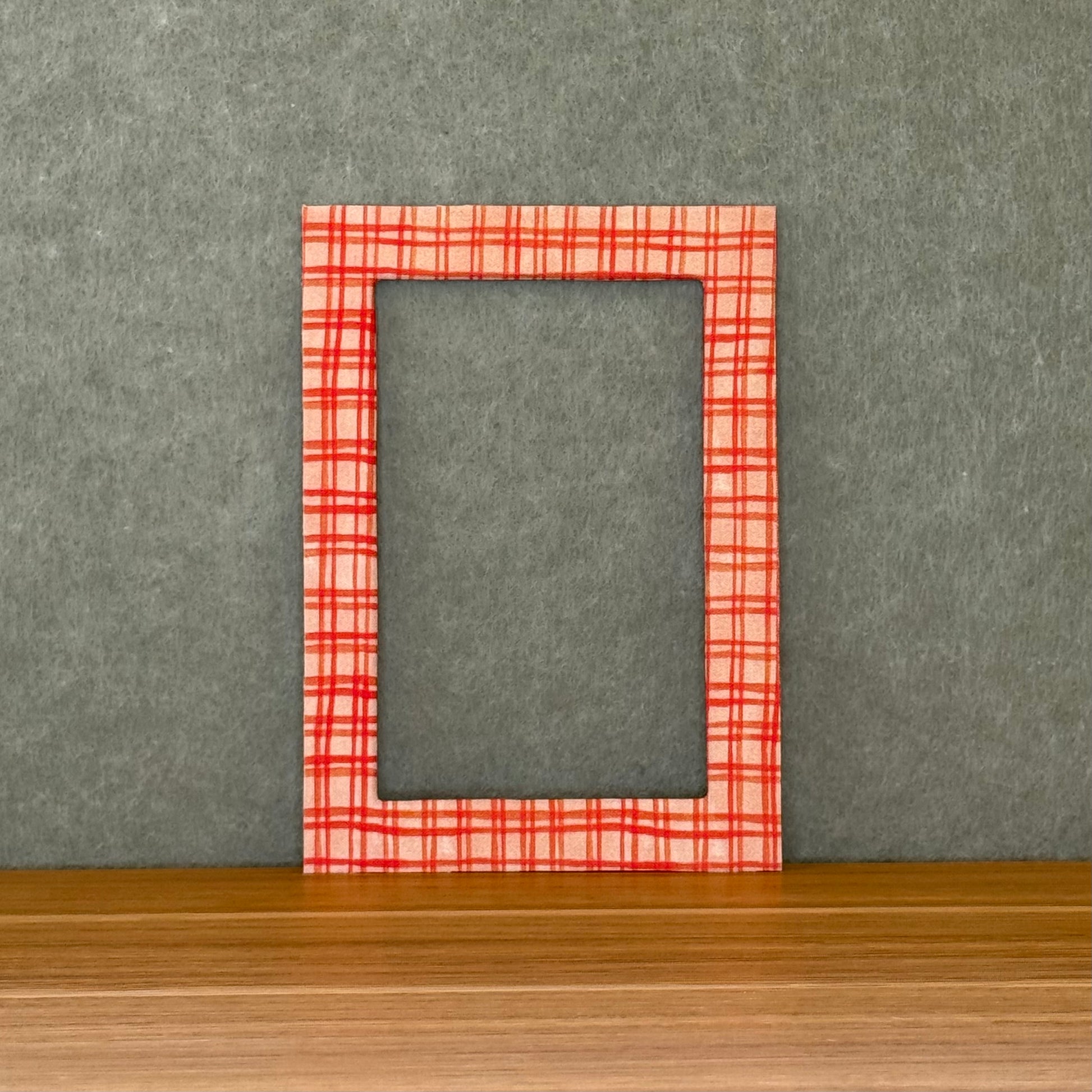 Red plaid photo mat on a wooden surface with a gray wall background. 