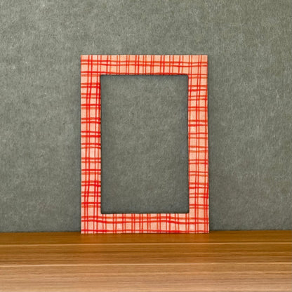 Red plaid photo mat on a wooden surface with a gray wall background. 