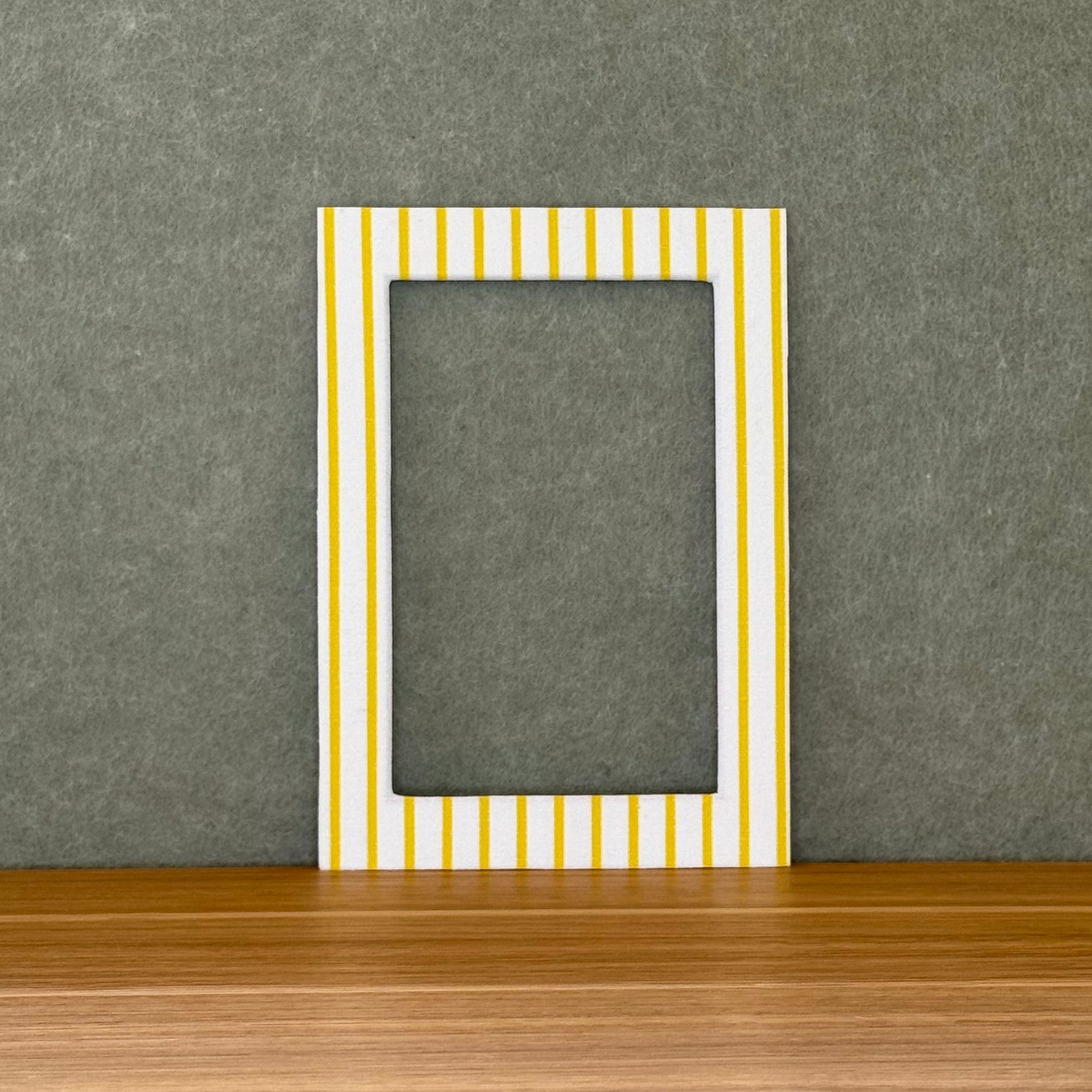 Striped photo mat with yellow and white stripes on a wooden surface with a gray wall background.