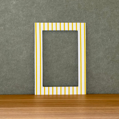 Striped photo mat with yellow and white stripes on a wooden surface with a gray wall background.