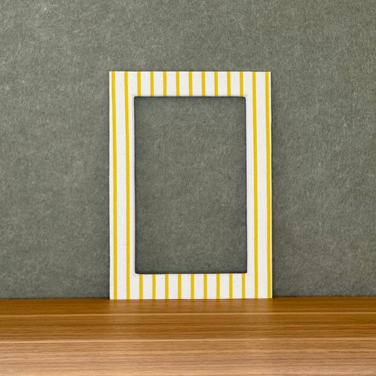 Striped photo mat with yellow and white stripes on a wooden surface with a gray wall background.