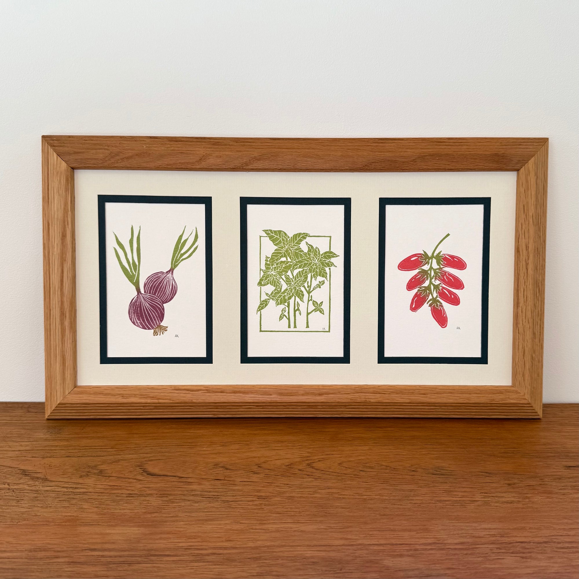 Framed artwork of onion, basil and tomatoes on a wooden surface with a white wall background