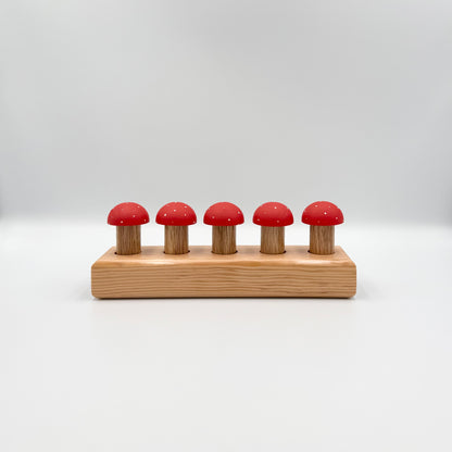 Red mushroom-shaped playing pegs sitting in a wooden block on a white background
