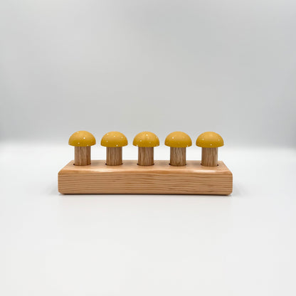 Yellow mushroom-shaped playing pegs sitting in a wooden block on a white background