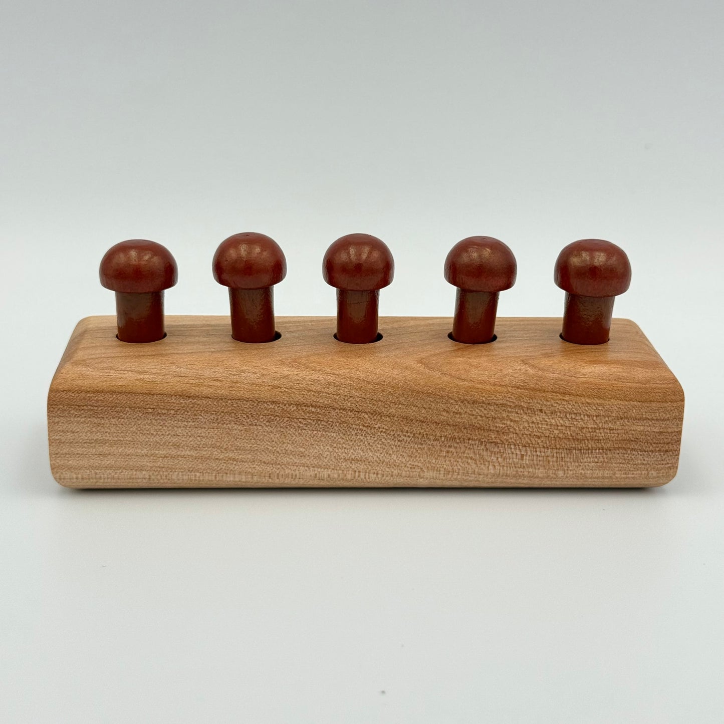 A wooden playing peg holder with dark rust color mushroom-shaped playing pieces, shown on a light gray background.